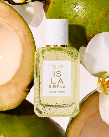 ISLA SIRENA Eau de Parfum 50ml next to whole and sliced coconuts and white flowers all covered in water droplets against a white background.
