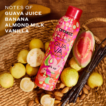 Amika x Ellis Brooklyn GUAVA GRANITA Perk Up Dry Shampoo in tan basket next to guavas, almonds, and vanilla beans on wooden table with bananas and white text that reads "notes of guava juice, banana, almond milk, vanilla"
