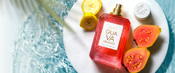 GUAVA GRANITA Eau de Parfum 50ml without cap lays next to cap, sliced guava and sliced bananas on a white plate all covered in water droplets against a background of blue water and green palm leaves