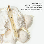 Vanilla Salt 10ml Eau De Parfum Travel Spray resting on whipped cream, vanilla ice cream, and pearl necklace, on white background next to black text that reads "Notes Of Sea Salt Accord, Whipped Cream, Madagascar Vanilla".