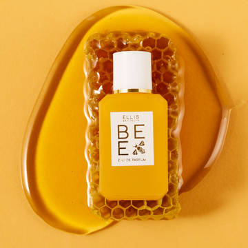 Bee 7.5ml Eau De Parfum Mini Dabber on piece of honey comb, in pool of honey, on yellow background.