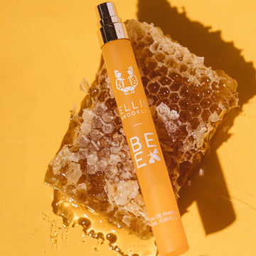 Bee 10ml Eau De Parfum Travel Spray with cap removed resting on piece of honey comb, on yellow background.